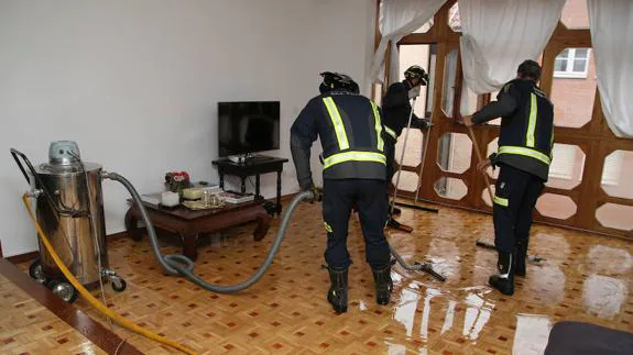Los bomberos achican el agua en el salón de una vivienda.