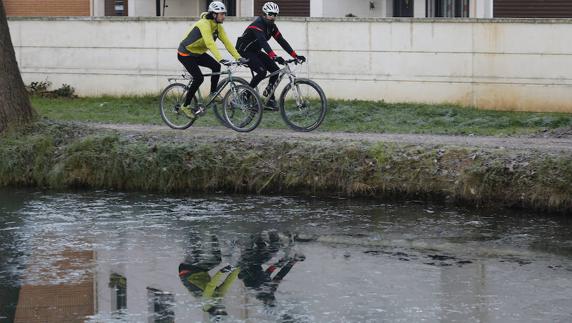 Dos ciclistas avanzan junto al Canal de Castilla helado. 
