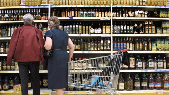 Clientes examinan las botellas de aceite de oliva alineadas en la estanterías de un centro comercial.