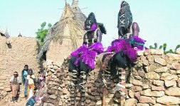 Dos danzantes dogón, con sus características máscaras y los pies calzados con zancos, descansan en una valla. / FOTOS: F. LÓPEZ SEIVANE