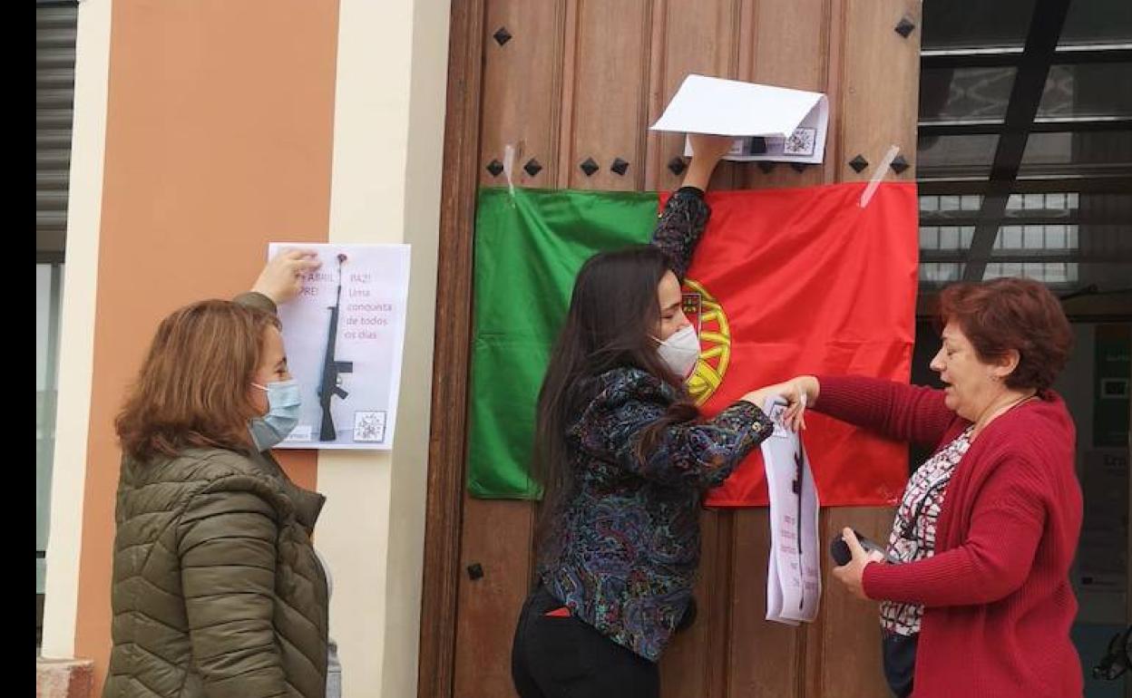 Unas profesoras colocan la bandera luso en la puerta de la escuela. 