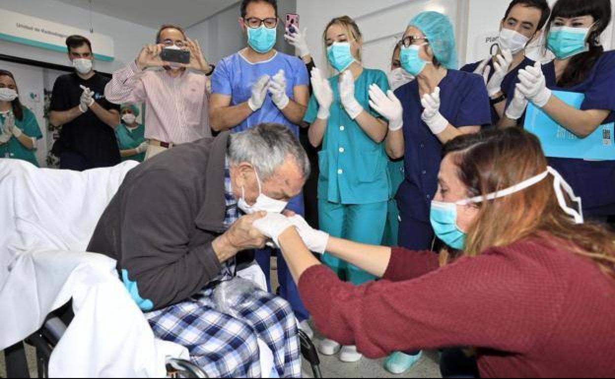 Feliciano Durán, de 85 años, besa las manos de su nieta mientras es aplaudido por el personal de la Clínica Quirón de Cáceres tras recibir el alta.