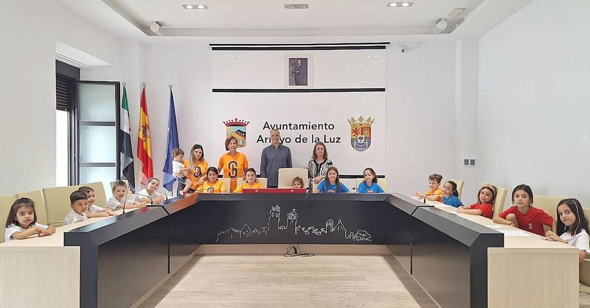 Los pequeños ocupando los sillones del Equipo de Gobierno en el Salón de Plenos, acompañado por sus monitores y el alcalde local.