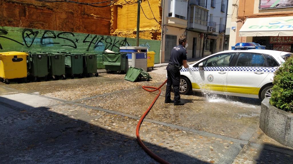 Uno de los agentes limpiando el lugar tras apagar las llamas e imagen del contenedor quemado.
