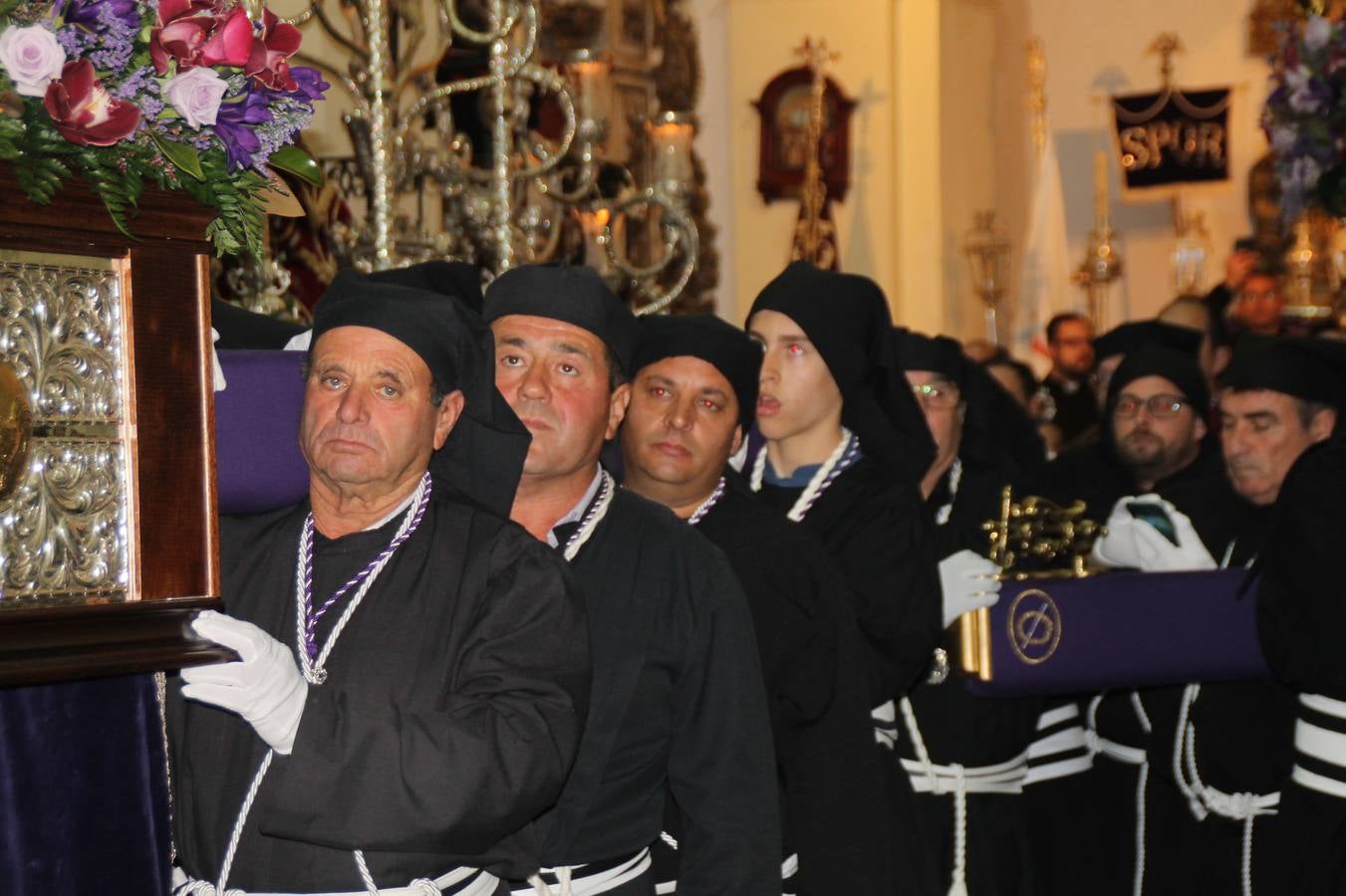 Las emociones llenaron también anoche la ermita de Los Santos Mártires, donde se quedaron guardados todos los afanes, las ilusiones y la devoción que no pudieron tener reflejo en la procesión de las colas largas, La Cofradía del Señor Coronado de Espinas decidió no salir ante la adversidad de la climatología y en el interior de este pequeño templo se vivieron momentos de gran emotividad.La Guardia Civil de Jerez de los Caballeros rindió honores a s Madrina, María Santísima de la Amargura. Los sones de las bandas y agrupaciones que iban a participar en el desfile procesional expandieron su eco desde el Llano de los Mártires para acompañar a los costaleros de cada uno de los tres Pasos, que fueron mecidos a su compás. El jovencísimo saetero Julián Jaramillo, de tan solo 12 años y natural de Segura de León, hizo vibrar a los presentes con su saeta al Coronado.Y entre las oraciones del párroco, Antonio María Rejano y los sacerdotes que le acompañaron, asomaron también las lágrimas.El momento más emotivo se vivió con el sentido homenaje a Manuel Labrador González, Manolo 'Cornelio' a quien Marisa Sánchez, en nombre de la junta de gobierno de la Cofradía del Señor Coronado, dedicó palabras llenas de afecto y reconocimiento, destacando su condición de «trabajador sin igual», su carácter innovador, su generosidad, sus consejos a jóvenes y mayores en el seno de esta Cofradía de la que dijo, «es piedra angular» y su extraordinaria labor. Manuel recibió un libro y una precioso cartel realizada por José Tomás Pérez Indiano, a semejanza del que hace tres años anunció la Semana Santa Jerezana. Emocionado, Manuel agradeció el cariño y dedicó este homenaje a su familia y a todas las madres.
