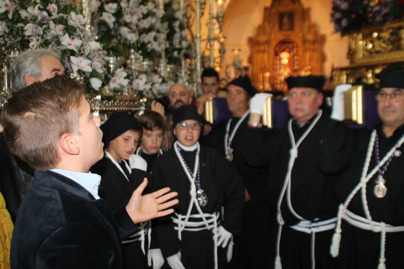 Las emociones llenaron también anoche la ermita de Los Santos Mártires, donde se quedaron guardados todos los afanes, las ilusiones y la devoción que no pudieron tener reflejo en la procesión de las colas largas, La Cofradía del Señor Coronado de Espinas decidió no salir ante la adversidad de la climatología y en el interior de este pequeño templo se vivieron momentos de gran emotividad.La Guardia Civil de Jerez de los Caballeros rindió honores a s Madrina, María Santísima de la Amargura. Los sones de las bandas y agrupaciones que iban a participar en el desfile procesional expandieron su eco desde el Llano de los Mártires para acompañar a los costaleros de cada uno de los tres Pasos, que fueron mecidos a su compás. El jovencísimo saetero Julián Jaramillo, de tan solo 12 años y natural de Segura de León, hizo vibrar a los presentes con su saeta al Coronado.Y entre las oraciones del párroco, Antonio María Rejano y los sacerdotes que le acompañaron, asomaron también las lágrimas.El momento más emotivo se vivió con el sentido homenaje a Manuel Labrador González, Manolo 'Cornelio' a quien Marisa Sánchez, en nombre de la junta de gobierno de la Cofradía del Señor Coronado, dedicó palabras llenas de afecto y reconocimiento, destacando su condición de «trabajador sin igual», su carácter innovador, su generosidad, sus consejos a jóvenes y mayores en el seno de esta Cofradía de la que dijo, «es piedra angular» y su extraordinaria labor. Manuel recibió un libro y una precioso cartel realizada por José Tomás Pérez Indiano, a semejanza del que hace tres años anunció la Semana Santa Jerezana. Emocionado, Manuel agradeció el cariño y dedicó este homenaje a su familia y a todas las madres.