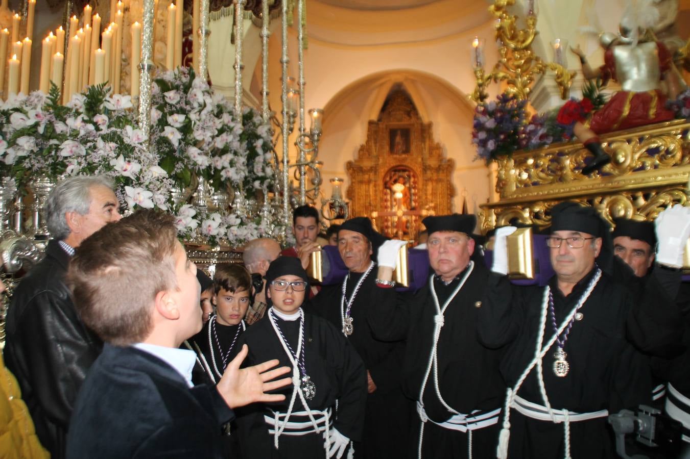 Las emociones llenaron también anoche la ermita de Los Santos Mártires, donde se quedaron guardados todos los afanes, las ilusiones y la devoción que no pudieron tener reflejo en la procesión de las colas largas, La Cofradía del Señor Coronado de Espinas decidió no salir ante la adversidad de la climatología y en el interior de este pequeño templo se vivieron momentos de gran emotividad.La Guardia Civil de Jerez de los Caballeros rindió honores a s Madrina, María Santísima de la Amargura. Los sones de las bandas y agrupaciones que iban a participar en el desfile procesional expandieron su eco desde el Llano de los Mártires para acompañar a los costaleros de cada uno de los tres Pasos, que fueron mecidos a su compás. El jovencísimo saetero Julián Jaramillo, de tan solo 12 años y natural de Segura de León, hizo vibrar a los presentes con su saeta al Coronado.Y entre las oraciones del párroco, Antonio María Rejano y los sacerdotes que le acompañaron, asomaron también las lágrimas.El momento más emotivo se vivió con el sentido homenaje a Manuel Labrador González, Manolo 'Cornelio' a quien Marisa Sánchez, en nombre de la junta de gobierno de la Cofradía del Señor Coronado, dedicó palabras llenas de afecto y reconocimiento, destacando su condición de «trabajador sin igual», su carácter innovador, su generosidad, sus consejos a jóvenes y mayores en el seno de esta Cofradía de la que dijo, «es piedra angular» y su extraordinaria labor. Manuel recibió un libro y una precioso cartel realizada por José Tomás Pérez Indiano, a semejanza del que hace tres años anunció la Semana Santa Jerezana. Emocionado, Manuel agradeció el cariño y dedicó este homenaje a su familia y a todas las madres.