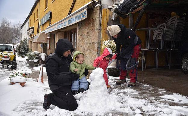 Unos padres juegan con sus hijos en la nieve junto a la N-110, Tornavacas.