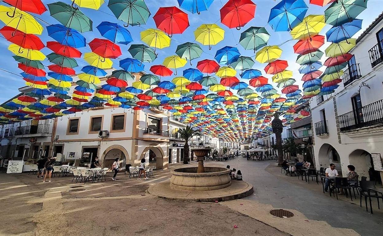 Varias personas disfrutan bajo los icónicos paraguas de colores de Malpartida de Cáceres. 