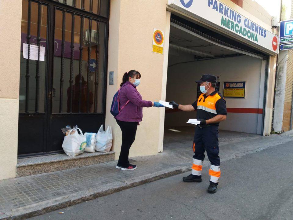Uno voluntario de Protección Civil entrega un díptico a una vecina a la entrada de un supermercado 