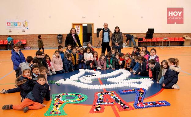 Escolares el polideportivo junto a la paloma de la paz dibujada con tapones 
