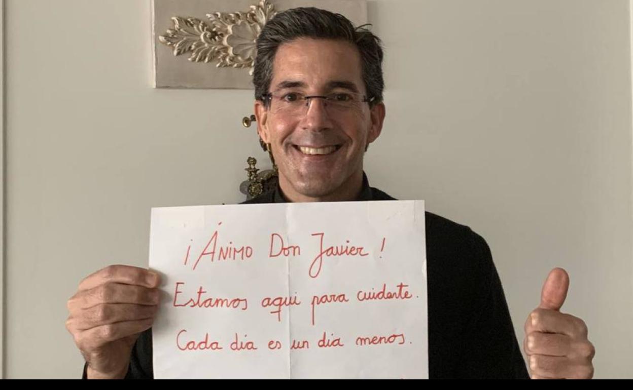 El sacerdote Javier Aguas posa con el cartel que le dejaron los sanitarios durante su ingreso en el hospital. 