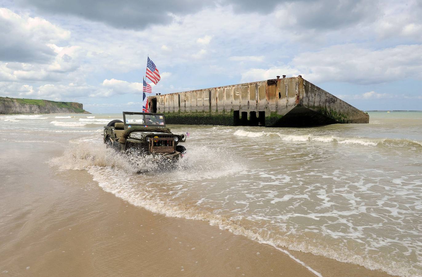 Un hombre francés vestido con ropa militar de época lleva un viejo jeep militar estadounidense en la playa en Arromanches-les-Bains, al norte de Francia,. AFP PHOTO / JEAN FRANCOIS MONIER