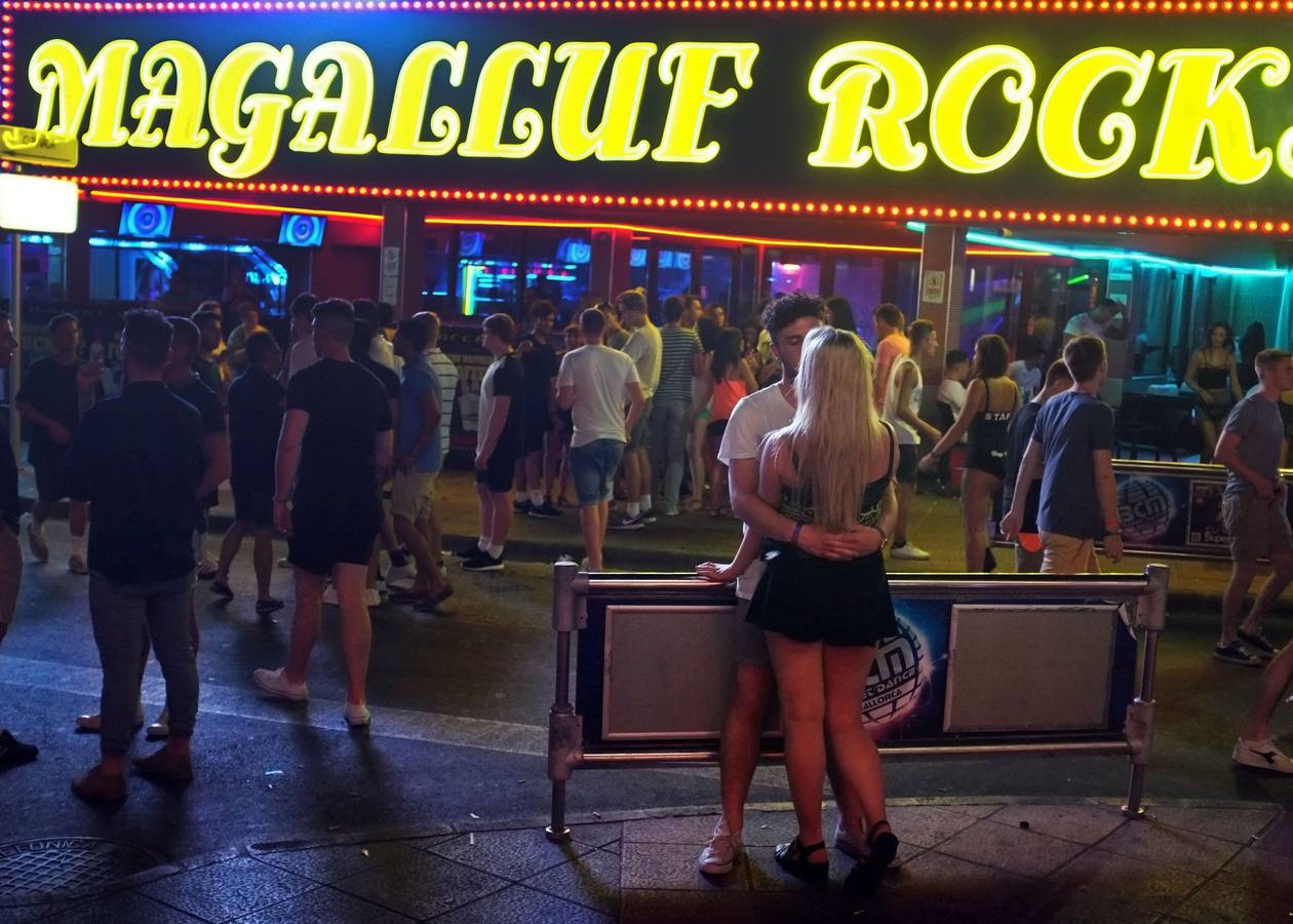 Una pareja se besanen frente de un club de la calle Punta Ballena en Magaluf, Mallorca.