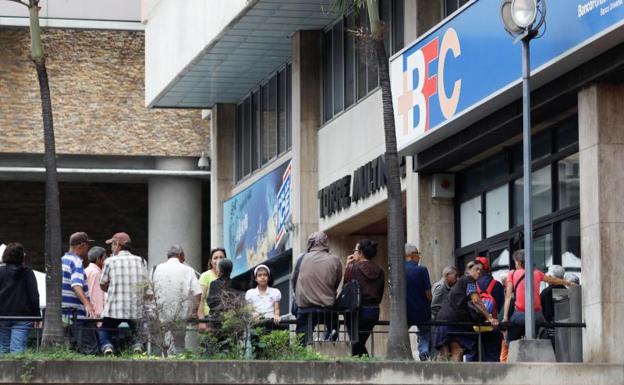 Varias personas esperan ante una sucursal bancaria en Caracas.