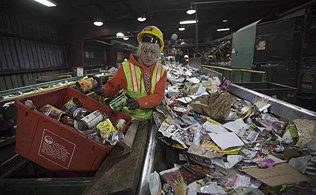 Una operaria de una planta estadounidense de tratamiento de residuos clasifica la bnasura que corre por una cinta transportadora.