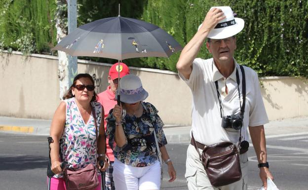 Turistas de Burgos caminan protegidos del sol en Mérida.