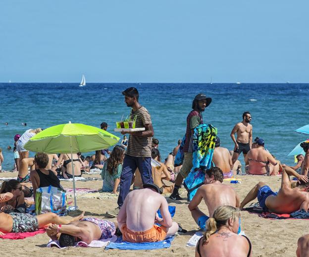 Ocio y negocio. Un vendedor de mojitos se cruza con otro de pareos en la playa de la Barceloneta