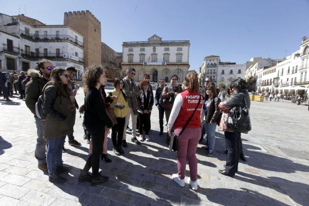 Un grupo de turistas atiende las explicaciones de un guía en la plaza Mayor de Cáceres. :: L. Cordero