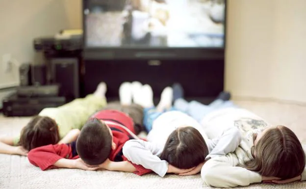 Varios niños ven la televisión tumbados en el suelo. 