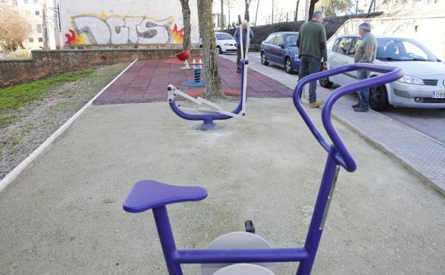 Dos equipos de gimnasia para personas mayores y al fondo, un muelle balancín y un carrusel giratorio para los niños.