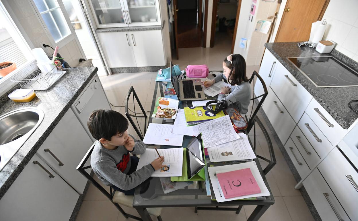 Dos niños haciendo los deberes en la mesa de la cocina.