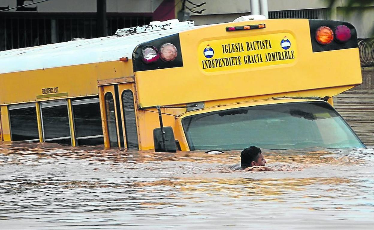 Una persona nada junto a un autobús semihundido para ponerse a salvo en una zona inundada por el ciclón.