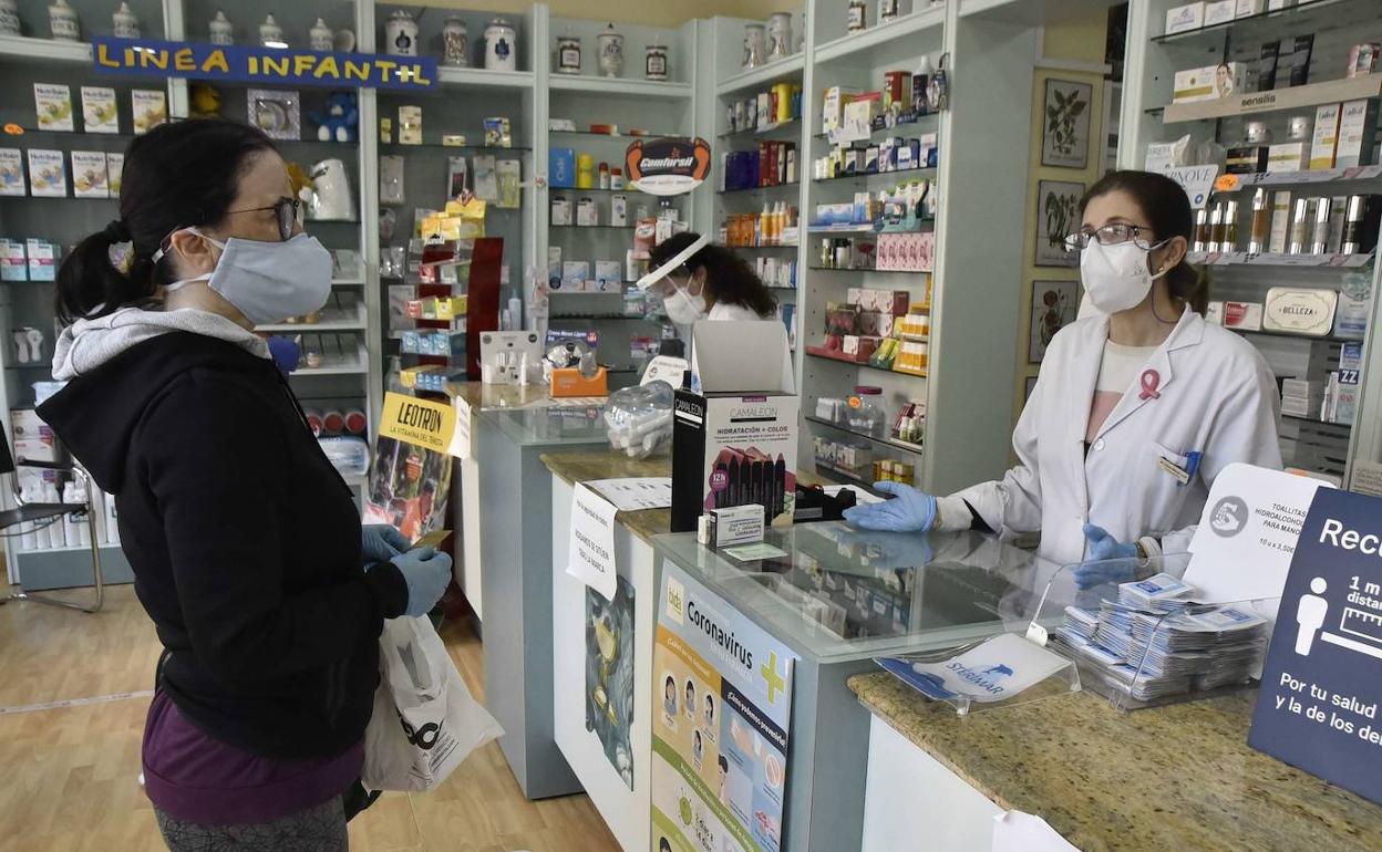 Una farmacéutica de Badajoz atiendie a una clienta a distancia y con mascarilla.
