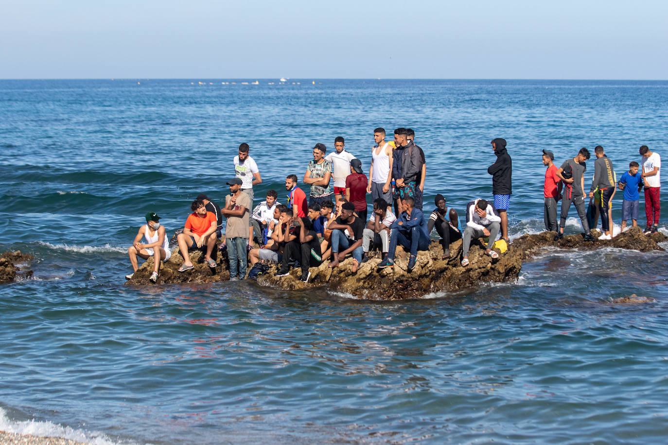 Migrantes aguardan en unas rocas frente a la playa de El Tarajal. 