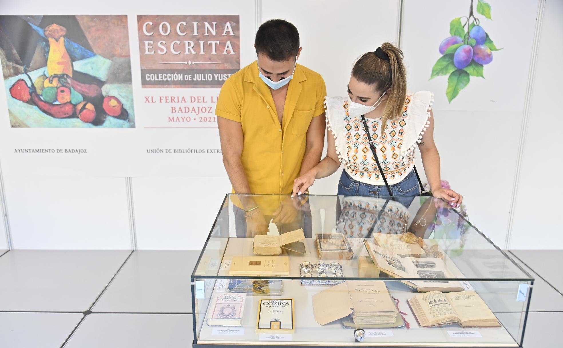 Dos jóvenes viendo la exposición dedicada a los libros de cocina de la Unión de Bibliófilos de Extremadura en la Feria del Libro. 