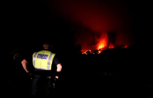 La lava fluye junto a un policía local tras la erupción del volcán.