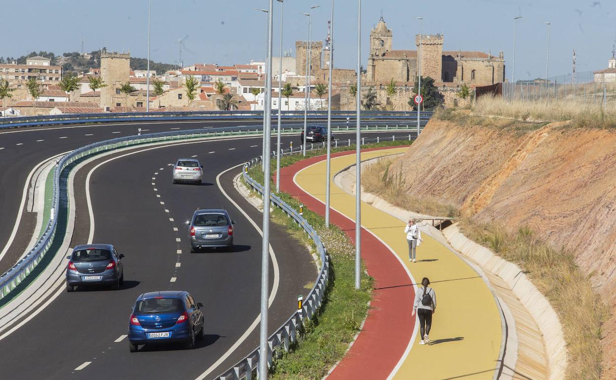 Varios coches circulan por la ronda sureste en dirección a San Marquino, con dos personas paseando por el carril peatonal. 