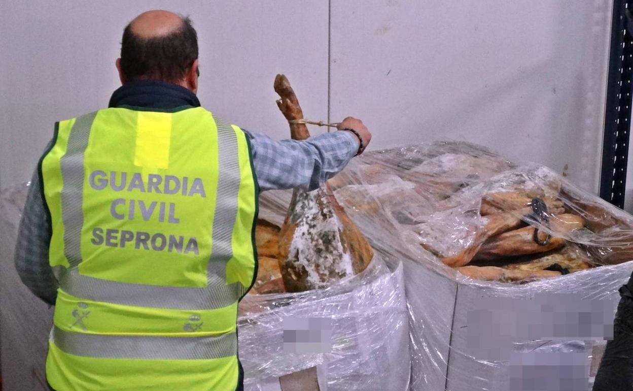 Un agente del Seprona junto a jamones decomisados en una nave. 