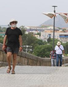 Imagen secundaria 2 - Arriba, una mujer camina con un gorro esta mañana en Badajoz. Abajo, a la izquierda, una joven se protege del sol con un paraguas. A la derecha, dos hombres por el Puente Romano de Mérida con sombrero