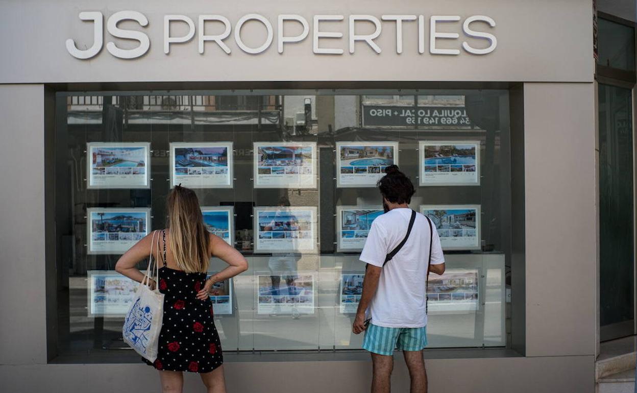 Dos jóvenes consultan ofertas de viviendas en una inmobiliaria. 