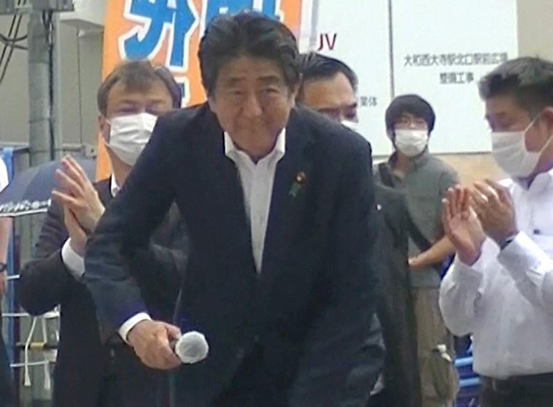 Shinzo Abe se dirige a ofrecer el mitin con su asesino observándole al fondo a su espalda 