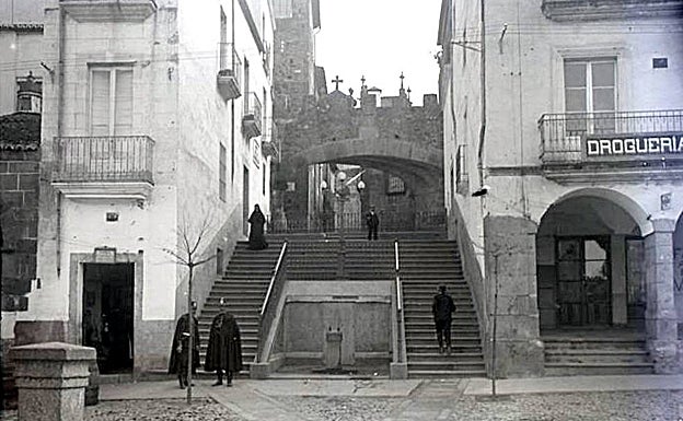 Una de las dos imágenes de una fotografía estereoscópica de la escalera del Arco de la Estrella de Cáceres, con una fuente y dos guardias de principios del siglo XX. 