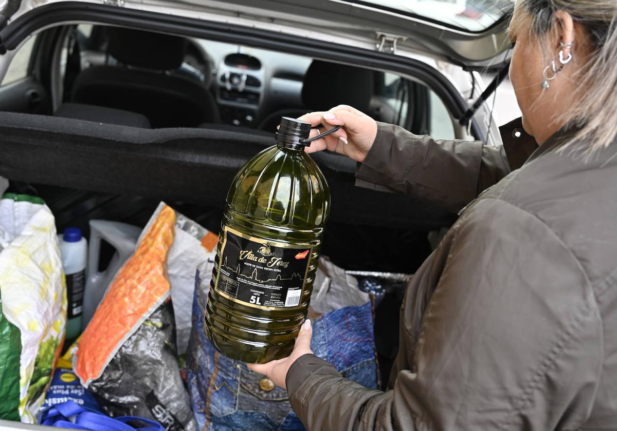 Una mujer carga en el maletero de su coche una garrafa de aceite.