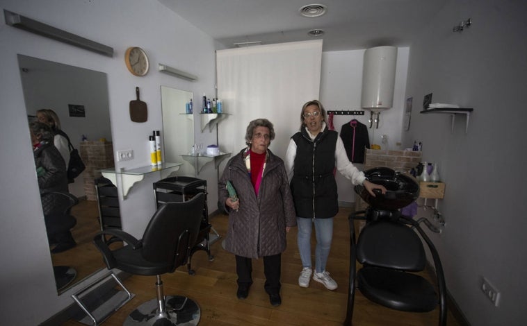 Imagen principal - Arriba, Laura Escobar, en la peluquería, con una clienta. Abajo, Antonio García, cliente del hogar de mayores, se dispone a abonar su consumición, ya con luz en el local. Abajo, una vecina abre la puerta del negocio.