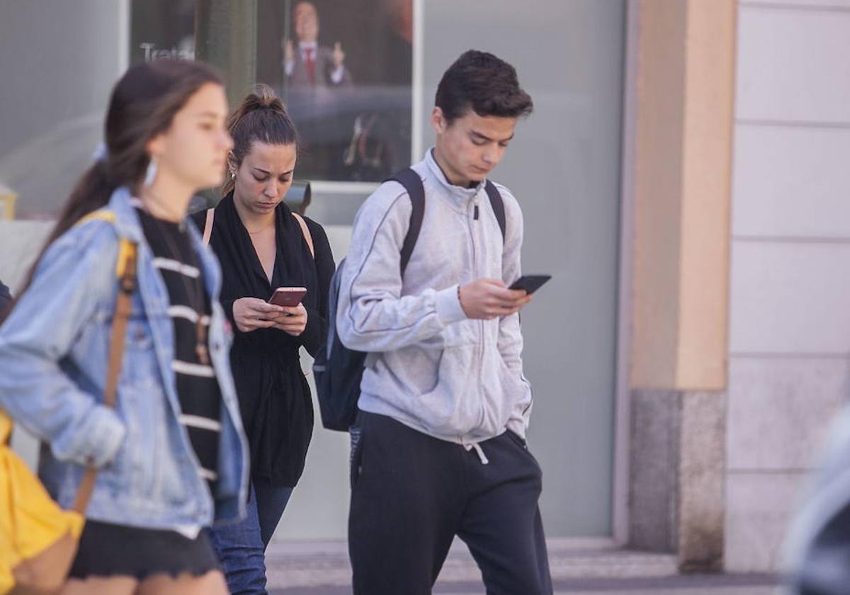 Jóvenes consultando el móvil por la calle.