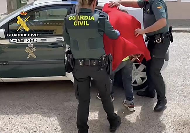 Dos agentes conducen a uno de los detenidos al coche de la Guardia Civil.