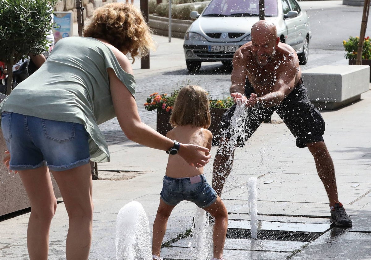 Unos padres refrescan a su hija con agua de una fuente próxima al Puente Romano de Mérida, una estampa habitual del verano emeritense.