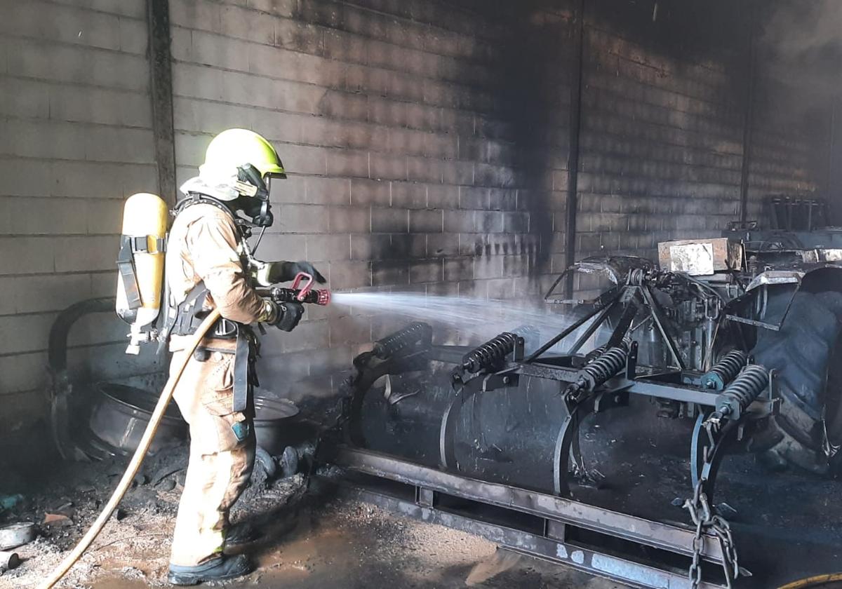 Un bombero del Sepei lanza agua sobre un tractor del interior de la nave.