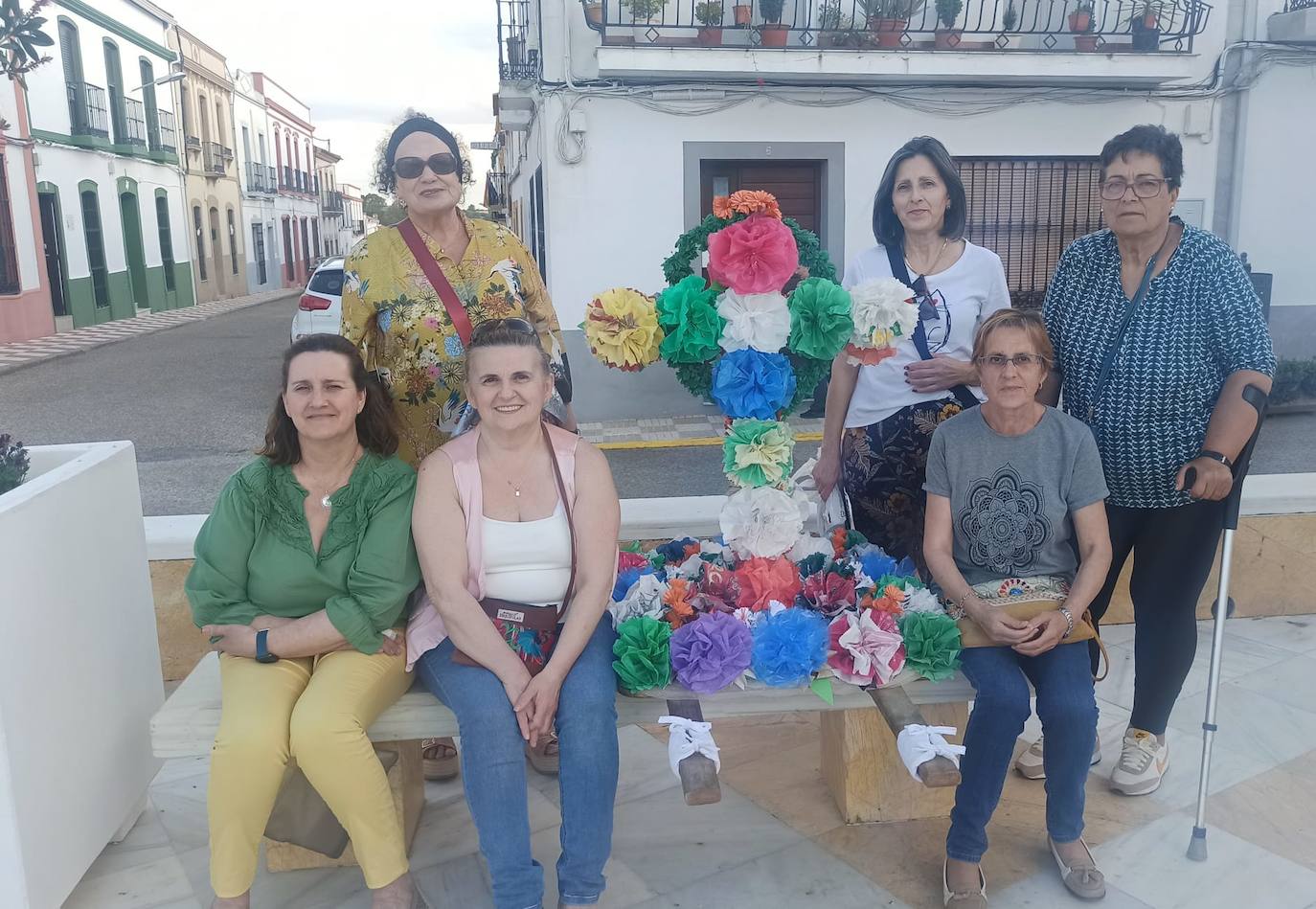 Imagen principal - Arriba, mujeres de la asociación 'Amanecer', con su cruz hecha con flores de bolsas de plástico. Abajo, componentes de la asociación 'La Esperanza' con su cruz, y la niña Marina García Correa, con una cruz tradicional en silla.