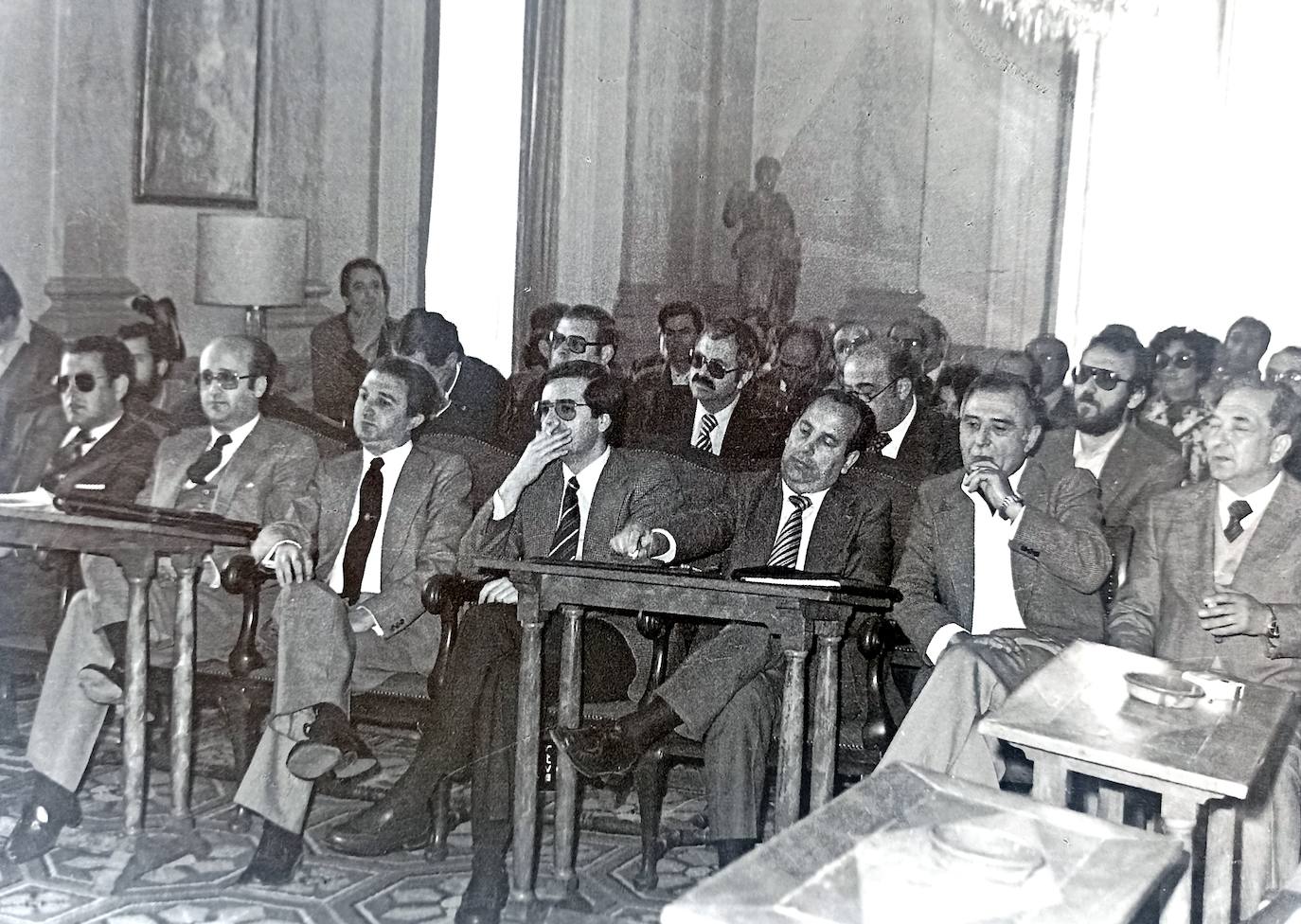 Salón de Plenos del Ayuntamiento de Cáceres el 19 de abril de 1979 para elegir el alcalde. En primer plano parte de los nuevos concejales, detrás los periodistas y público. Entre los concejales están Bazaga, Jaime Velázquez, Manuel Domínguez Lucero y Luis González Cascos; entre los periodistas están Manuel Carmona, Tomás Pérez, Fernando García Morales y Pepe Higuero. Por cierto, casi todos están fumando.