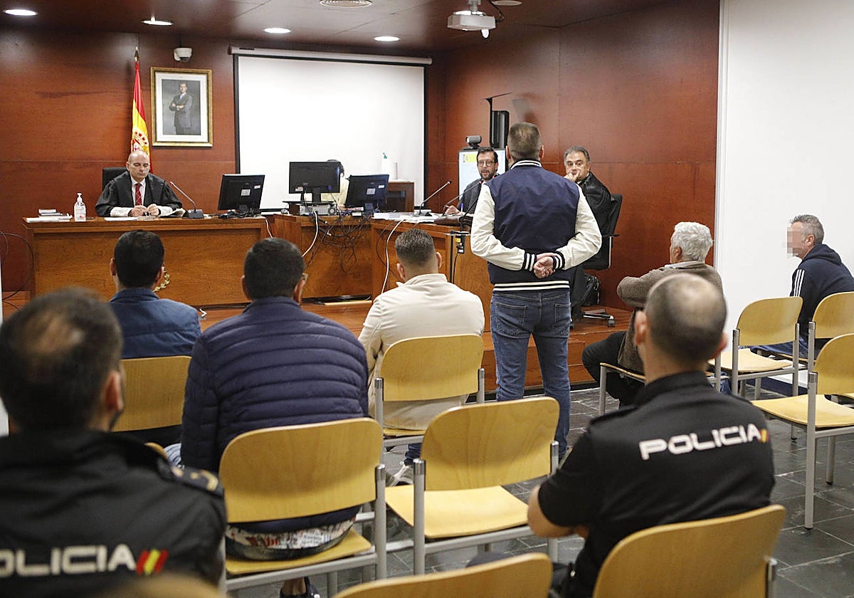 Los cinco acusados, junto a agentes de la policía, escuchando a un testigo.