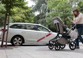 Una mujer empuja un carrito de bebé y pasa por delante de un taxi estacionado en la avenida de España de Cáceres.