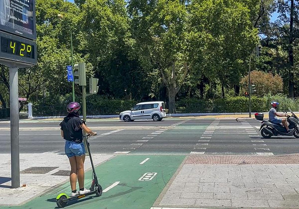 Una joven cirucla en patinete ante un cartel en el que se pueden ver los 42 grados.
