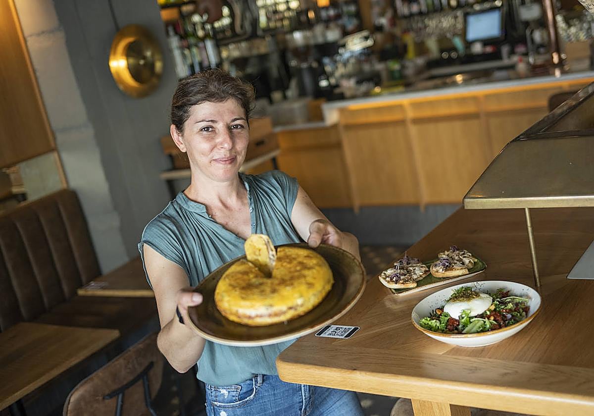 Elena sosteniendo algunos de los mejores platos de la nueva carta, con la tortilla de patatas fluida en cabeza.