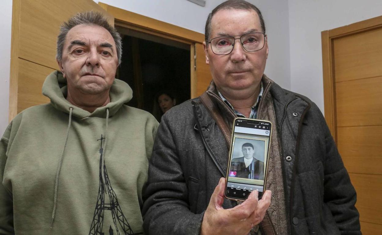 Los hermanos Domingo y Antonio Gutiérrez muestran en el móvil el retrato de su abuelo Domingo, uno de los extremeños fallecidos en la localidad vizcaína de Orduña, este sábado, en Castuera. 